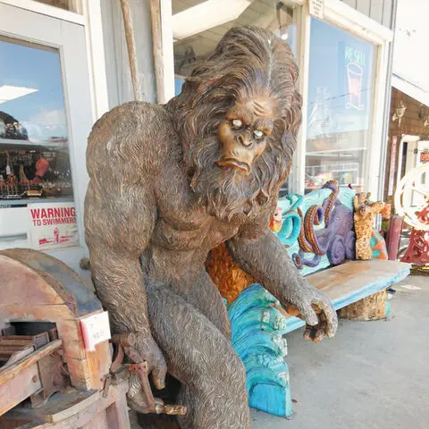 A wooden carved statue of Bigfoot stands outside a building.