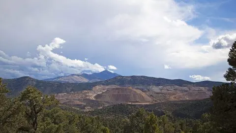 An open-pit mine in a mountainous landscape under a cloudy sky.