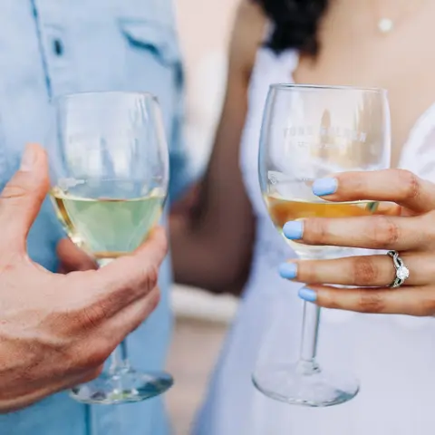 Two people hold glasses filled with white wine.