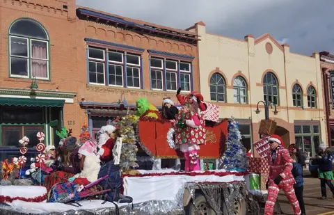 A Christmas parade float passes down a street lined with historic brick buildings.