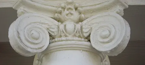 A close-up of a white architectural column capital with intricate carvings.