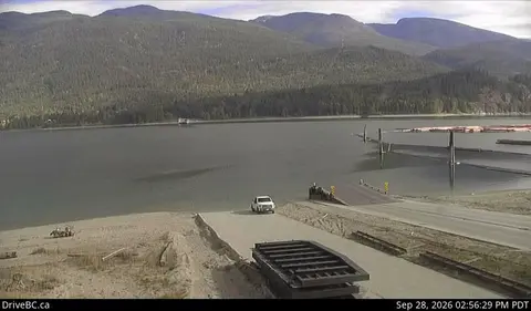 A view of a lake and mountains from a boat ramp with a vehicle parked nearby.