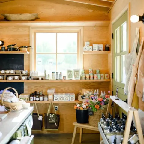 An interior view of a small shop with wooden shelves displaying various goods, a window, and a green door.