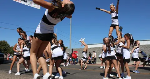 A group of young cheerleaders perform stunts outdoors on a street.