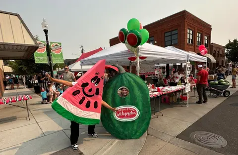 People in watermelon costumes stand on a downtown street during an event.