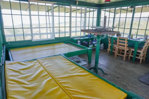 The interior of a fire lookout tower with windows, beds, and a finder table.
