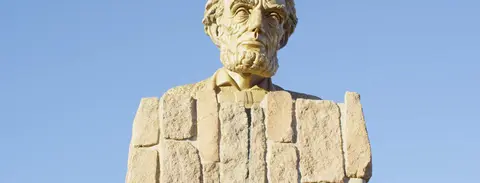 A stone bust of a bearded man against a blue sky.