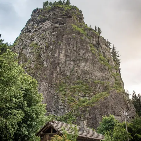 A massive rock formation towers over a small wooden cabin with a chimney.