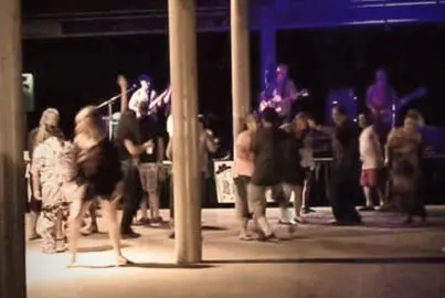 People dance at an indoor evening event with a band performing.