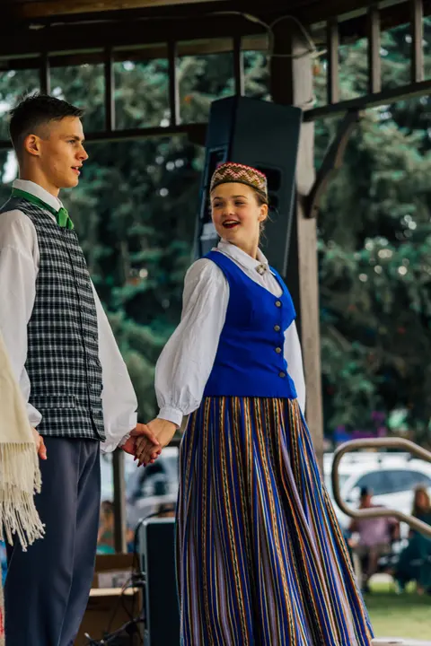 A young man and a woman in traditional costumes holding hands.