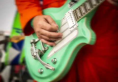 A close-up shot of a person playing a light green electric guitar.