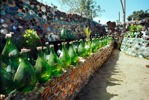 A stone wall inlaid with glass bottles with many green glass bottles displayed on top.