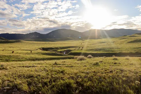 A scenic landscape view of grassy hills and mountains under a bright sun.
