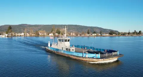 A ferry boat travels across a body of water with a shoreline and hills in the background.