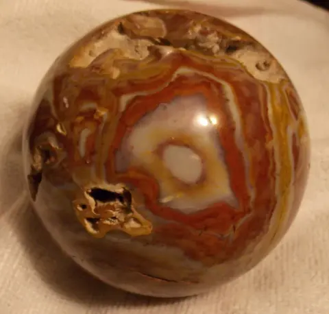 A polished sphere made of banded stone sits on a white surface.