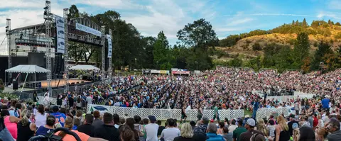 A wide-angle view of a large crowd attending an outdoor concert event.