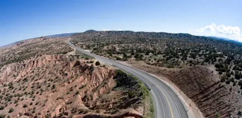 Aerial view of a paved road winding through a desert landscape with hills.