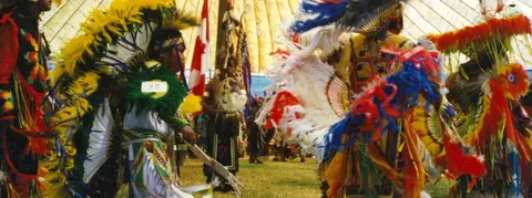 People in colorful regalia participate in a gathering inside a tent.