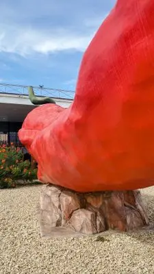 A large red pepper sculpture stands outdoors on a rock base.