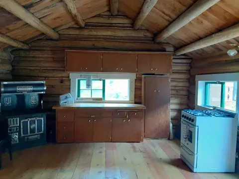 An interior view of a rustic log cabin kitchen with wooden cabinets and appliances.