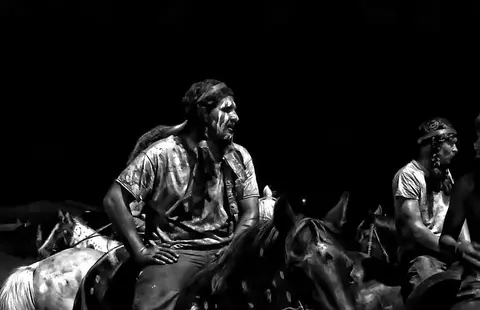 A black and white photo of people on horseback at night.