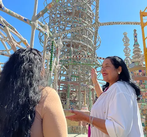 A woman points at an intricate outdoor structure while talking to someone.