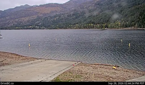 A concrete boat ramp leading into a wide lake surrounded by mountains and forests.