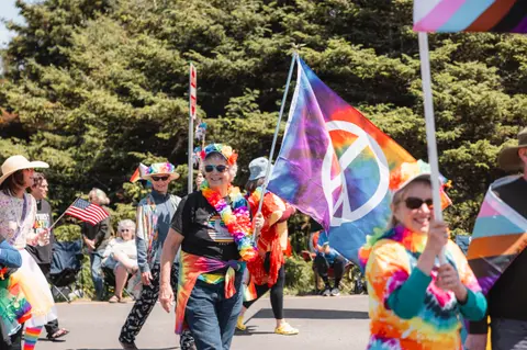 People participate in a colorful outdoor parade carrying flags and wearing leis.