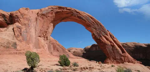 A large natural sandstone arch stands in a desert landscape under a blue sky.