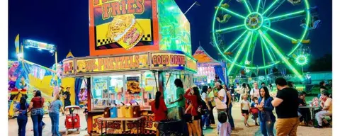 A night view of a brightly lit food stand and ferris wheel at a fair or carnival.