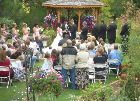 An outdoor wedding ceremony in a garden with seated guests watching.