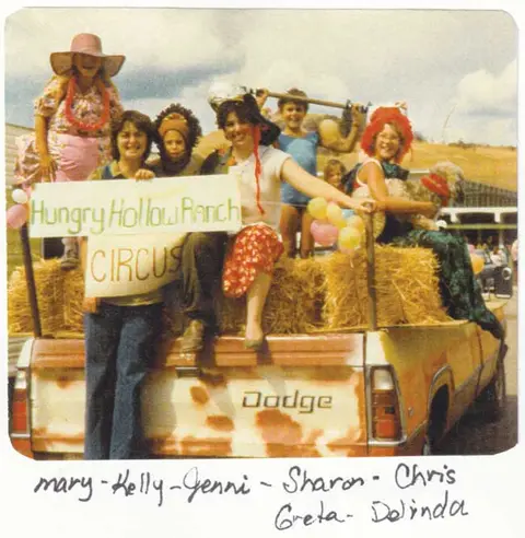 People in costumes on the back of a truck holding a circus sign.