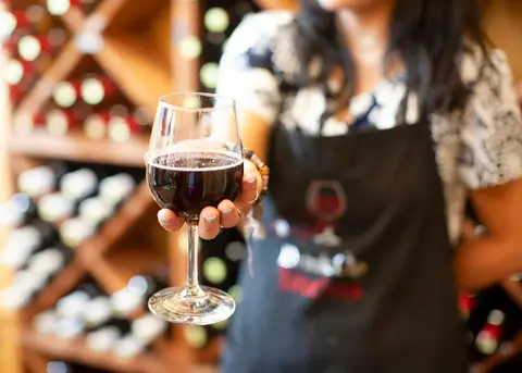 A person holds a glass of red wine indoors.