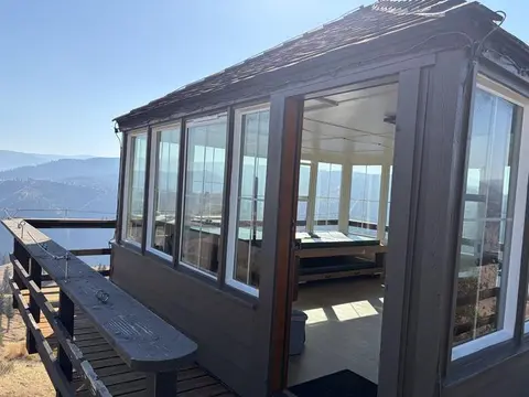 A wooden fire lookout cabin sits on a high elevation with a surrounding deck and mountain views.