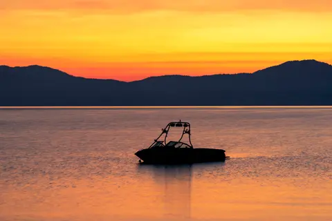 A boat silhouette on a calm body of water at sunset.