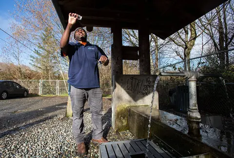 A man collects and tests a water sample from an outdoor water fountain.