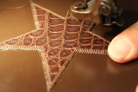A close-up view of a star-shaped piece of leather being sewn with a machine.