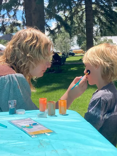 A person paints face art on a child outdoors.