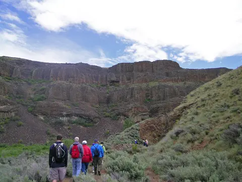 A group of people hiking on a trail near rocky cliffs.