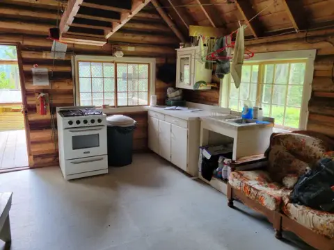 An interior view of a rustic cabin kitchen with a stove, counter, sink, and sofa.