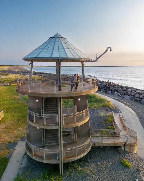 An exterior view of a multi-level observation tower near a coast with people standing on the top platform.