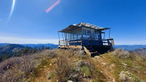 A fire lookout tower sits atop a mountain ridge under a clear blue sky.