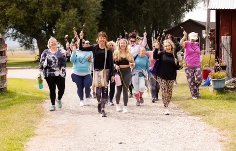 A group of women walk together on an outdoor path while holding small objects.
