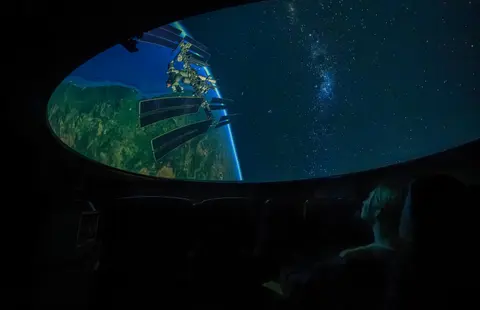 A person looks up at a dome projection of space and the Earth.