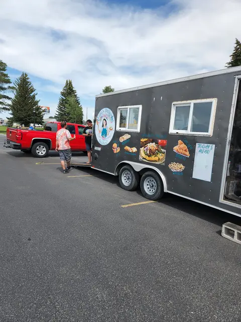 A food truck parked outdoors with a red pickup truck attached.