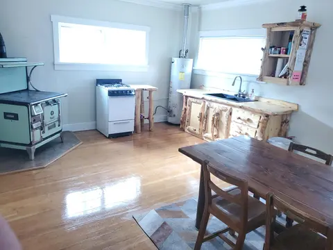 A rustic kitchen interior features a wood-burning stove, a modern range, a wooden counter with a sink, and a dining table.