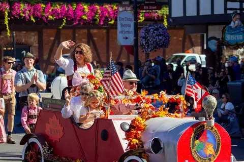 People in a parade ride in a decorated car waving to the crowd.