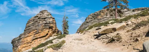 A person hiking up a rocky mountain trail under a blue sky.