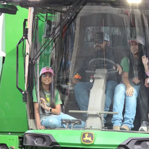 People sitting inside the cab of a green tractor.