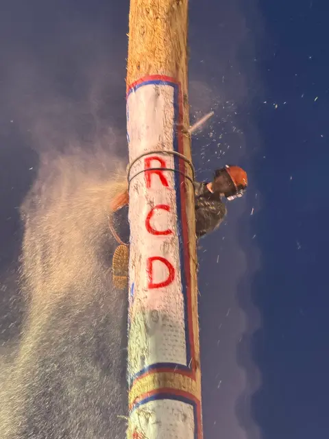 A person cuts a wooden pole with a chainsaw at night.